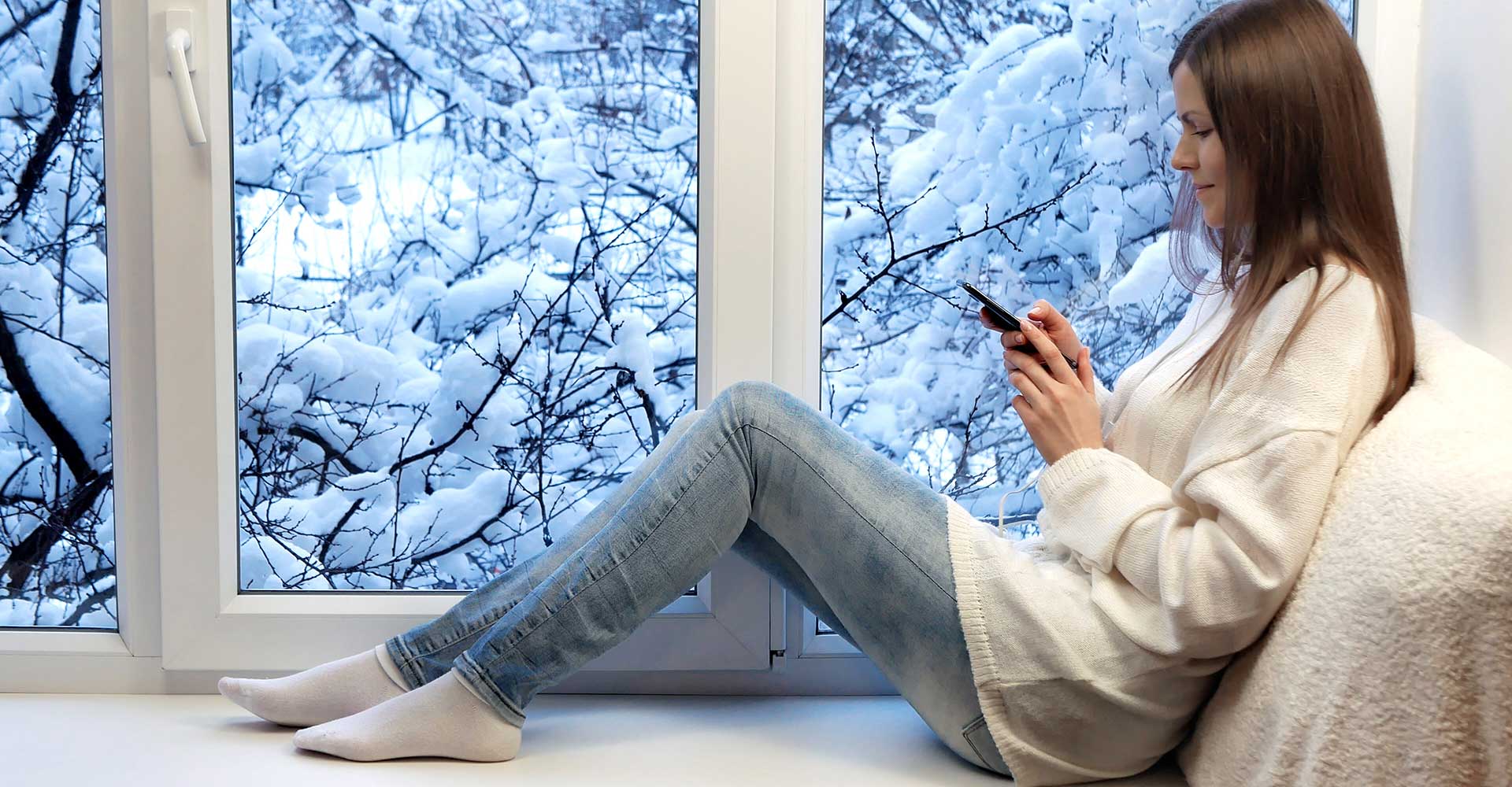 woman sitting on a window bench looking at her phone